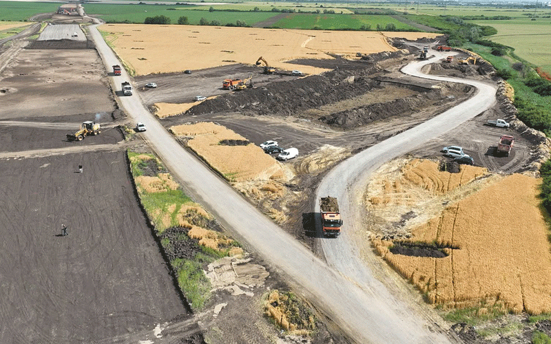 centura-vest7 - Sursa de Vest Aerial view of a rural road construction site with dirt roads, trucks, and excavators among farmland fields.