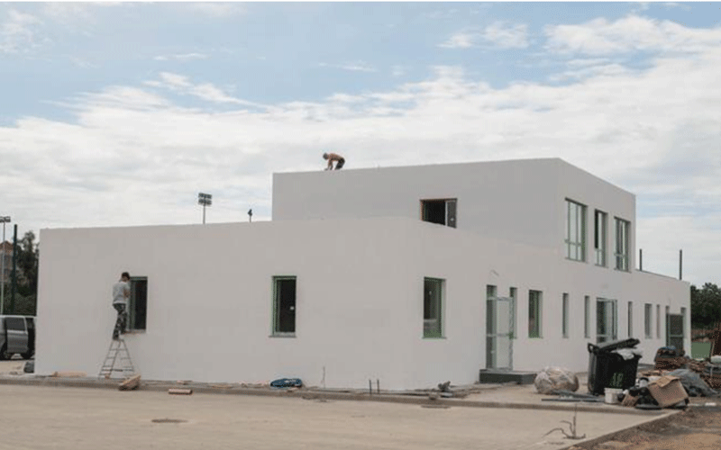 White modern building under construction with workers on the roof and a ladder on the left side.