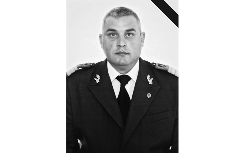 Black-and-white portrait of a man in formal military uniform with epaulettes and a mourning ribbon in the top-right corner, looking straight ahead.