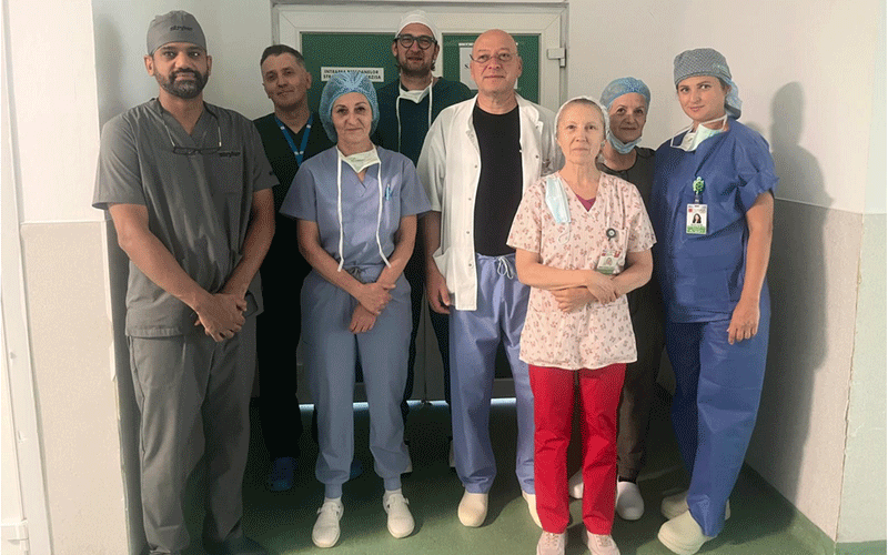 echipa-medicala-judetean - Sursa de Vest Group of healthcare professionals in scrubs posing for a team photo in a hospital corridor; doctors and nurses of mixed ages stand together.