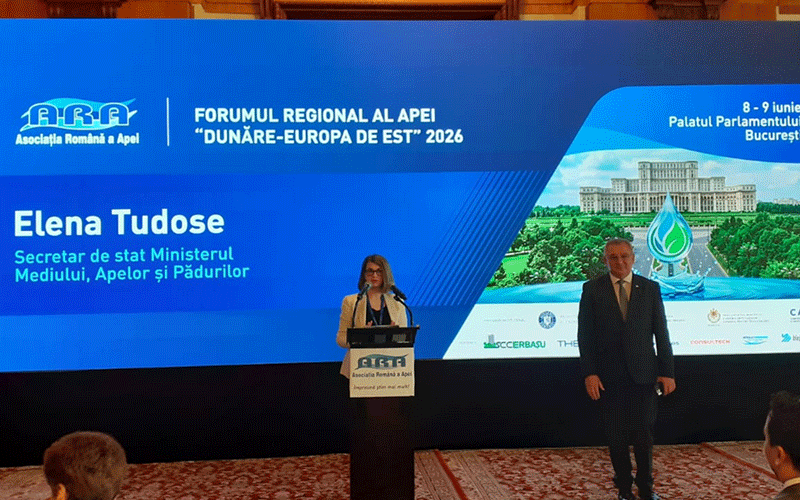forum-aquatim4 - Sursa de Vest Elena Tudose speaks at a podium during a regional forum in Bucharest, with a blue backdrop and a man in a suit beside her.
