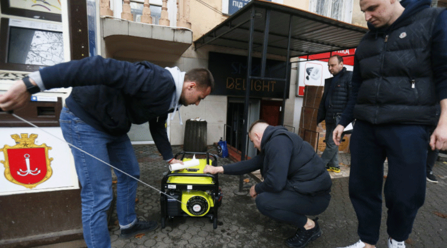 Three men on a sidewalk examine a small yellow portable generator, one bending over and one crouching nearby.