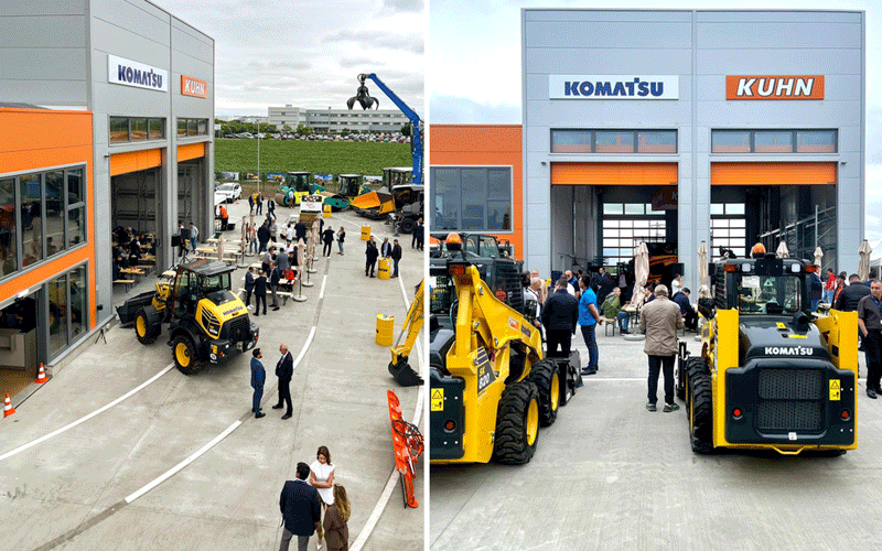 Outdoor construction equipment showroom event with people examining machines near a Komatsu/Kuhn building.