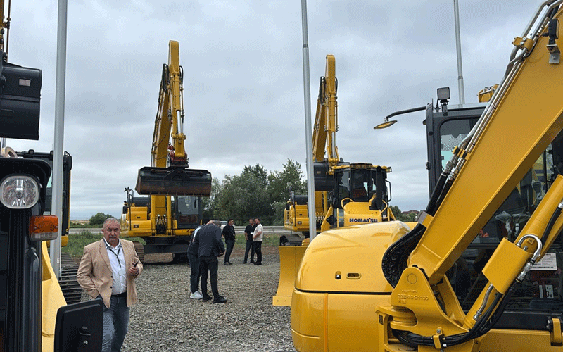 kuhn-romania - Sursa de Vest Group of people standing around large yellow excavators on a gravel lot under an overcast sky.
