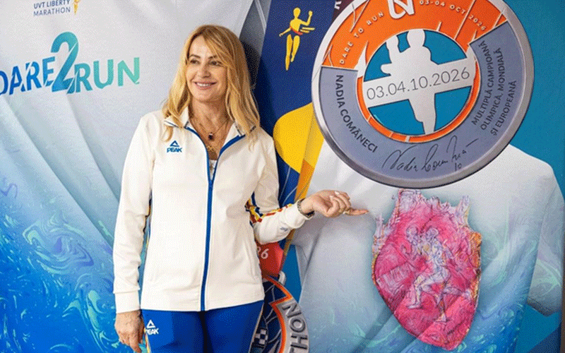 Smiling woman in a white athletic jacket and blue pants poses beside a large circular race medal cutout at a marathon event.