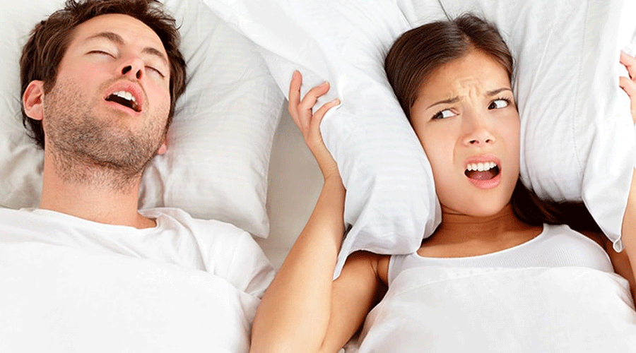 Couple in bed: man sleeping with mouth open while the woman looks alarmed under the pillows and blanket