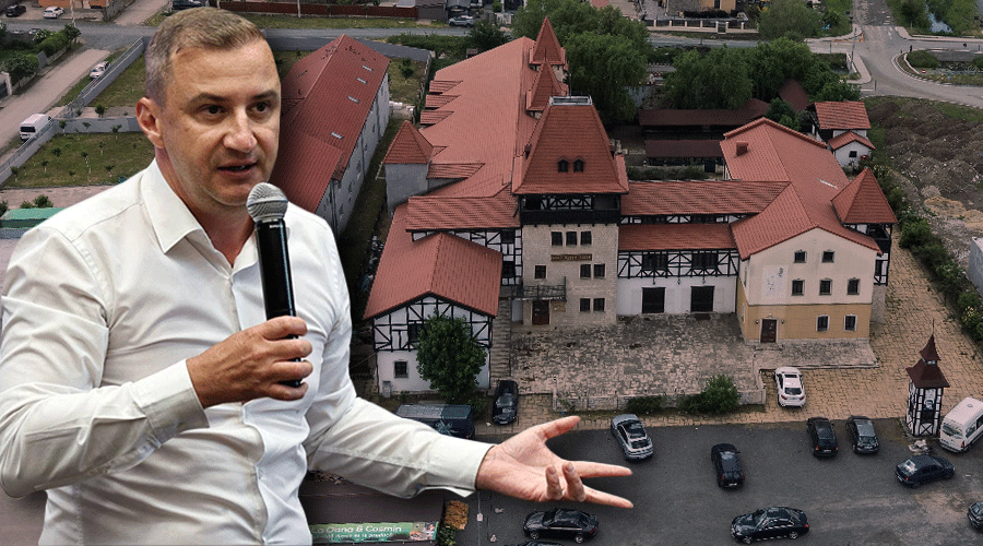 Man in a white shirt speaks into a handheld microphone in front of a red-roofed historic building complex viewed from above.