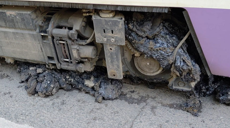 Underbody of a bus/tram with damaged wheel area and charred debris on the ground after an incident.
