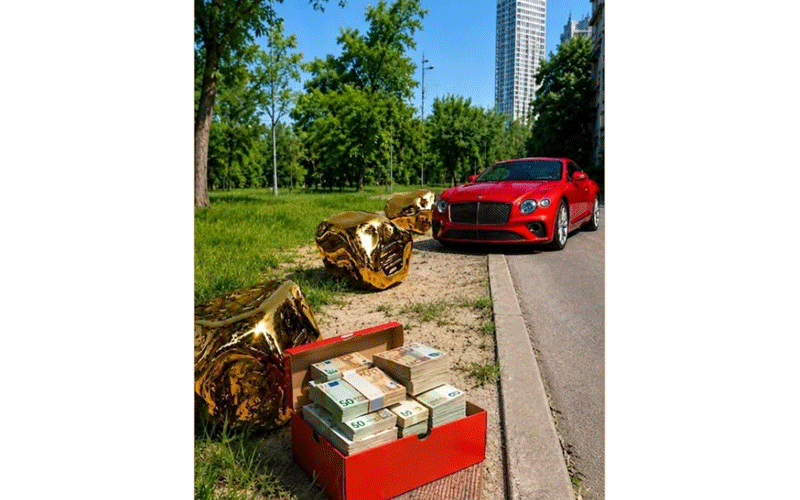 timisoara-in-viziunea-lui-simonis-usr-tineret - Sursa de Vest Red sports car parked by a park; an open red cash box with stacks of money sits on the sidewalk nearby, with large gold balloons in view.