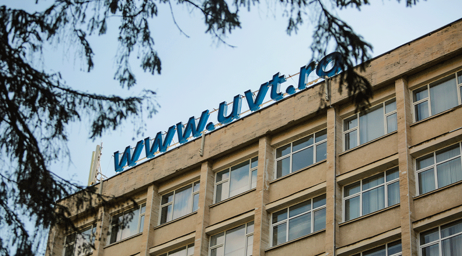 Beige four-story building with large windows and a blue 'www.uvt.ro' sign on the roof, tree branches partially framing the scene.