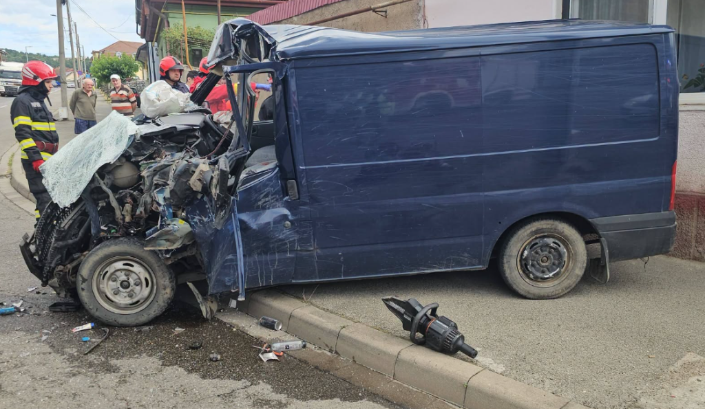 accident resita - Sursa de Vest Blue van with severe front-end crash on curb; firefighters and bystanders assess damage at the scene.