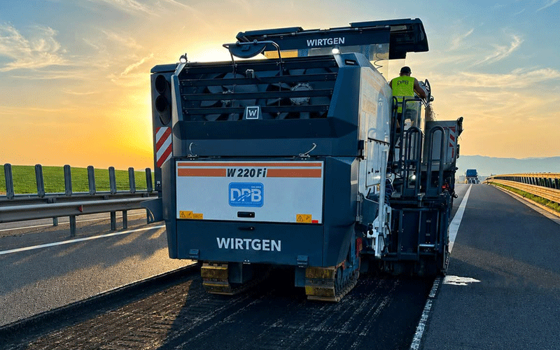 Wirtgen asphalt paver laying a new lane on a highway at sunset
