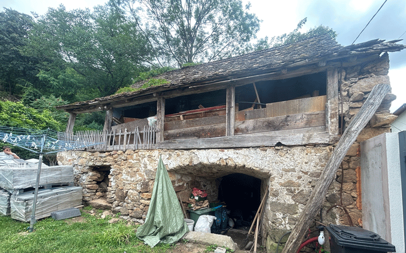 casa-caras - Sursa de Vest Dilapidated stone and wood house with a weathered upper balcony, set among trees and cluttered by the yard outside.