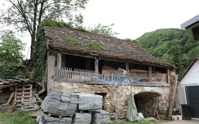 casa-caras3 - Sursa de Vest Old stone barn with a wooden balcony, ivy on the roof, and stacks of slate slabs in front.