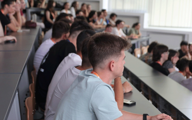 Students seated at long desks in a university lecture hall, attentively watching a presentation.