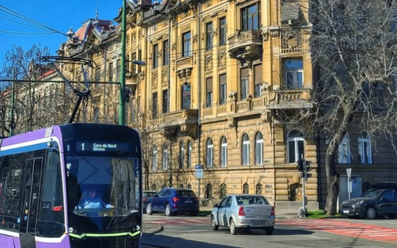 Purple tram on a city street with a historic yellow stone building and leafless trees in the background.