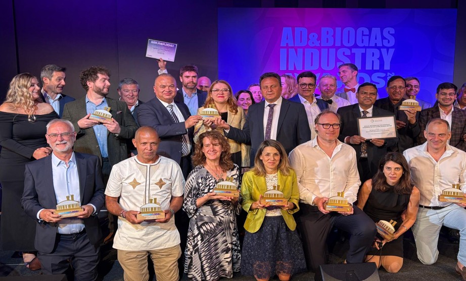usvt 1 - Sursa de Vest Group of men and women at an awards ceremony, each holding small trophy plaques in front of a blue stage backdrop and the event banner reading 'AD&BIOGAS INDUSTRY AWARDS'.