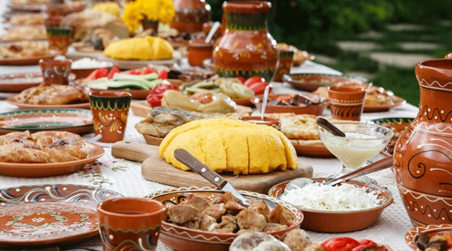 Outdoor table set for a feast with colorful ceramic pottery and a spread of breads, meats, and sauces.