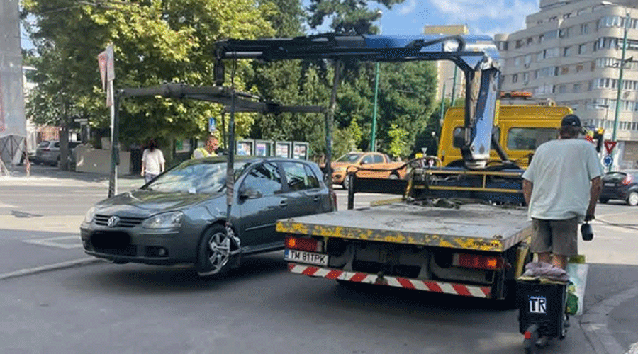Gray VW car being loaded onto a flatbed tow truck on a city street, with a man nearby.