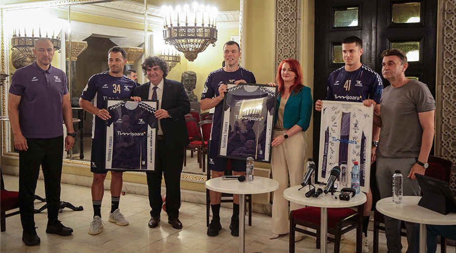 Group of six people at a press event, two athletes hold framed jerseys, microphones and water on tables nearby.