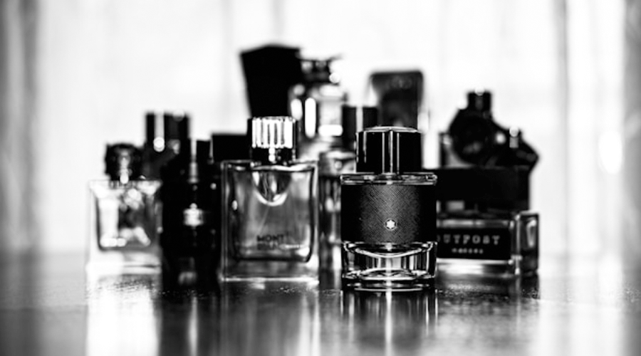 Black and white photo of assorted perfume bottles on a reflective surface in a shallow depth of field.