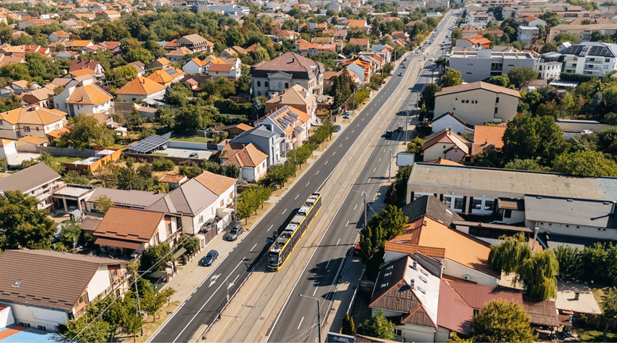 Aerial view of a suburban street with a tram running along the center between lanes of traffic and houses on both sides.