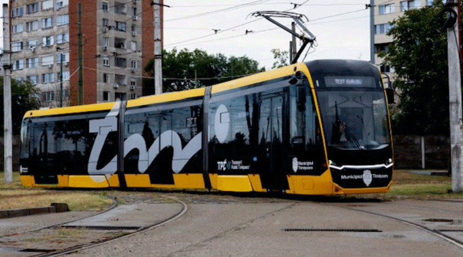 Yellow-and-black modern tram traveling on curved tracks through an urban area with apartment buildings nearby.