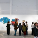 Group of people viewing abstract blue collage on a white gallery wall in a spacious room