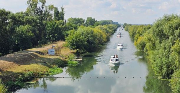 Boats cruising along a tree-lined canal with calm, reflective water viewed from above.