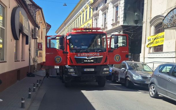 Red fire truck with open front doors blocking a narrow urban street; buildings line both sides and a yellow banner is visible on the right.