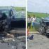 Two cars severely damaged in a head-on collision on a rural road; debris scattered, firefighters and bystanders on scene.