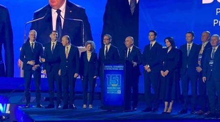 Group of formally dressed people on a stage at a conference, with a podium in the center.