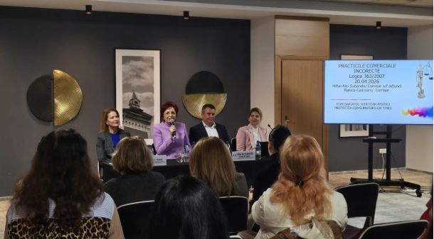 Panel discussion with four speakers seated at a long table, audience watching, and a slide projected on the right in Romanian.