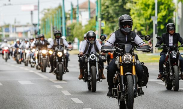Group of motorcyclists riding down a city street, front rider wearing a black helmet and vest.