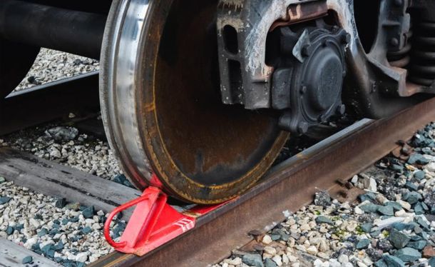 Close-up of a train wheel resting on the rail, with a red wedge wheel chock securing it