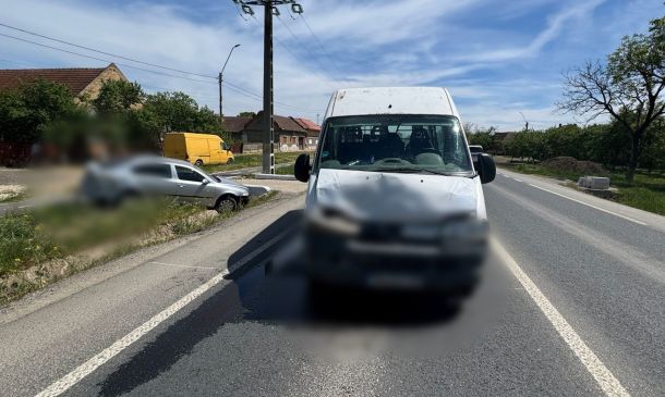 White van in the foreground on a two-lane rural road after an accident; blurred front bumper and a silver car off the left roadside, blue sky above.