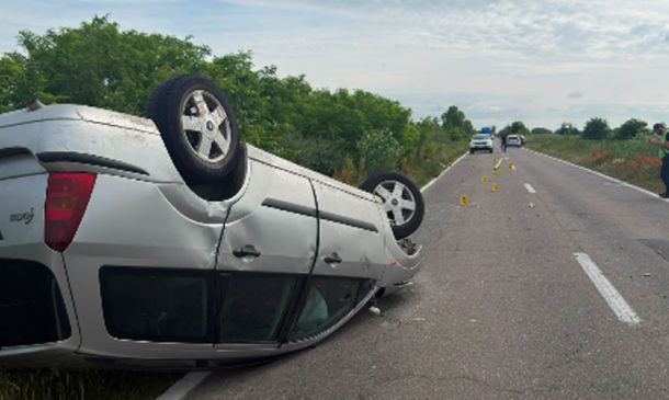 White SUV flipped onto its roof on a rural two-lane road; emergency responders and traffic cones visible in the distance.