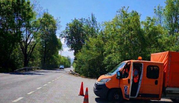 Orange maintenance van with open door parked on a tree-lined road, orange traffic cones in front signaling work ahead.