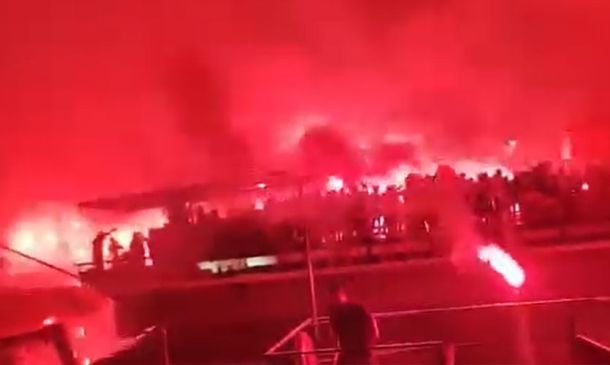 Crowd at night waving red flares, smoke lighting the scene in an intense red glow
