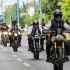 Group of motorcyclists riding down a city street, front rider wearing a black helmet and vest.