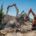 Two excavators demolish a concrete wall at a sunny construction site, dust rising over a pile of rubble; Primăria Municipiului Timișoara logo visible at the bottom.