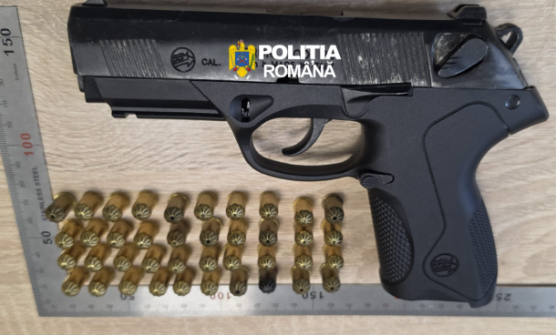 Black semi-automatic pistol with Romanian Police branding, placed on a wooden surface, with multiple brass cartridges arranged in rows below and a metal ruler for scale.