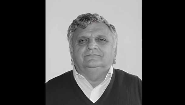 Portrait of a middle-aged man with gray hair wearing a white collared shirt and dark sweater, facing the camera.