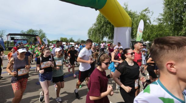 Group of runners starting a road race under a yellow inflatable arch, bib numbers visible on their shirts.