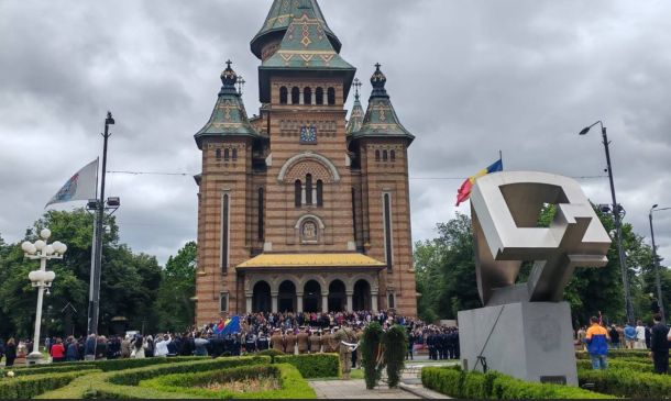 Brick church with green-tiled towers and a yellow awning; crowd gathered at entrance on a cloudy day.