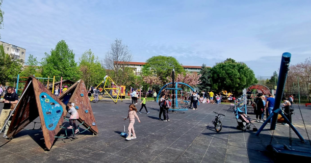 Wide view of a sunny public playground with wooden climbing frames and colorful play structures as children and adults explore.