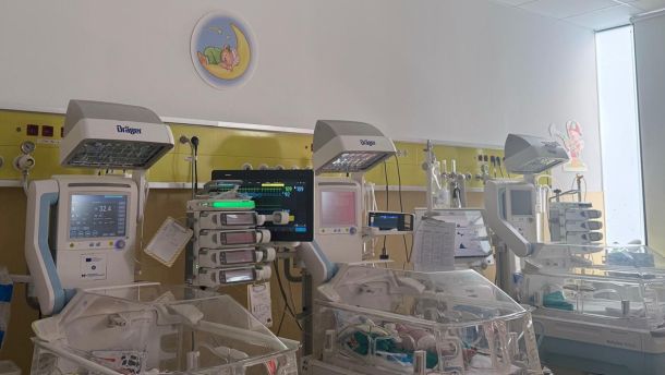 NICU room with several infant incubators and medical monitors mounted on a yellow wall panel.