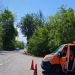Orange maintenance van with open door parked on a tree-lined road, orange traffic cones in front signaling work ahead.