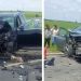 Two cars severely damaged in a head-on collision on a rural road; debris scattered, firefighters and bystanders on scene.