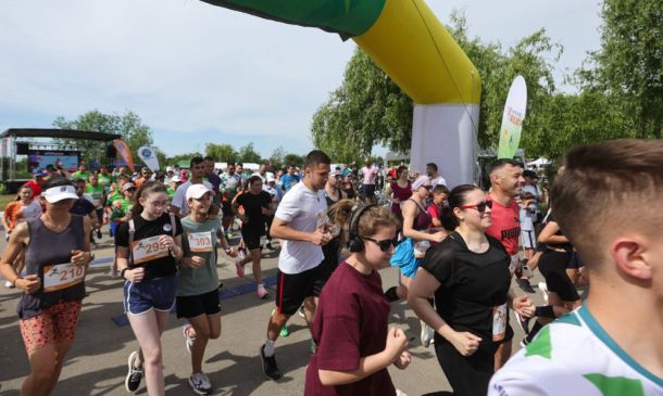 Group of runners starting a road race under a yellow inflatable arch, bib numbers visible on their shirts.
